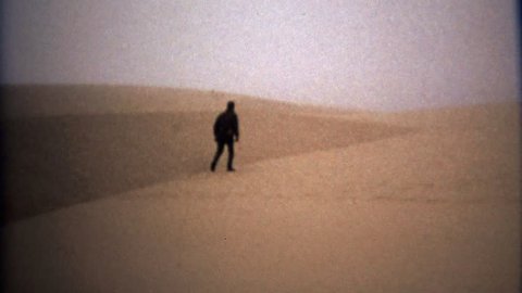 ASTORIA, OREGON 1971: Man walking in blonde yellow sand desert alien landscape.