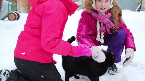 Two happy girls care black cat on snow at winter day