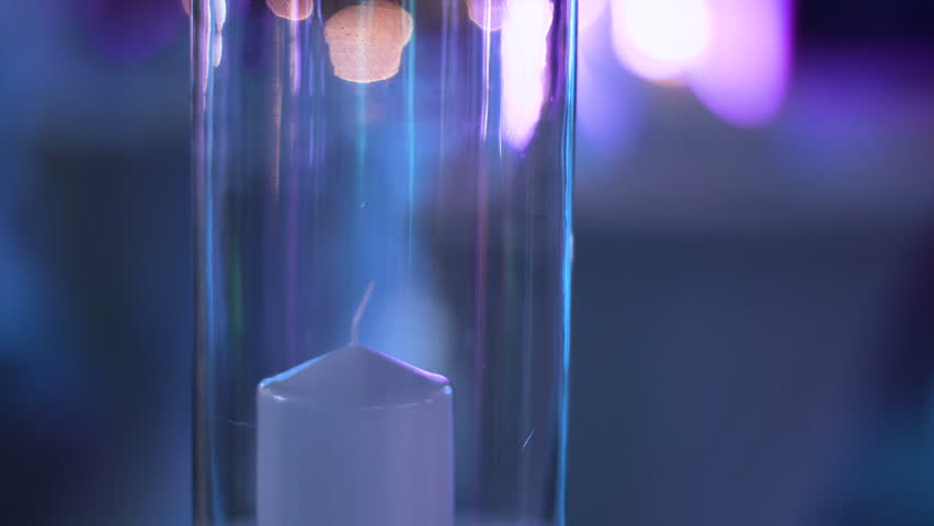 Detail footage of white decorative candle under a glass cup being flamed by a lighter.