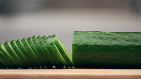Slicing cucumber and lettuce. Closeup of chopped vegetables on wooden cutting board. Stop motion animation, 4K.: film stockowy