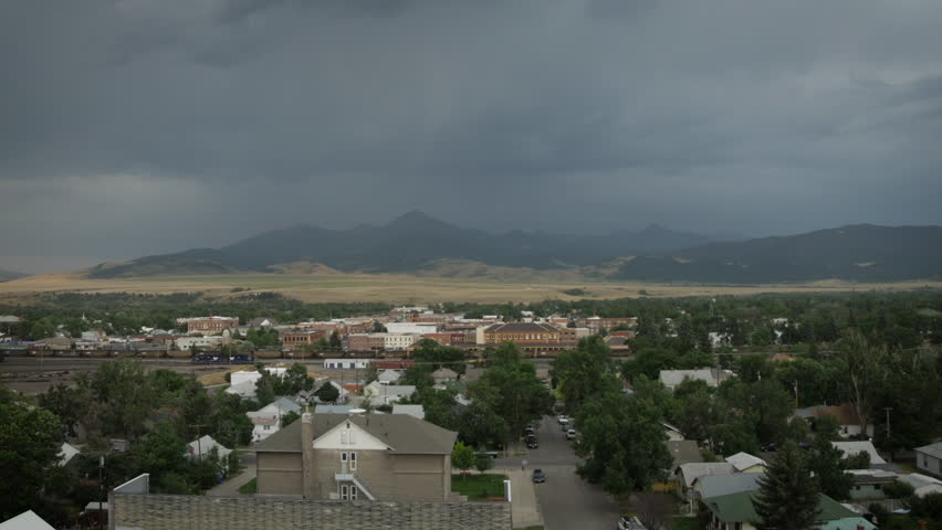 Static wide angle of small western train town on the Yellowstone River, Livingston, Montana with a long coal train passing through while storm clouds engulf the peaks in the distance P1030283