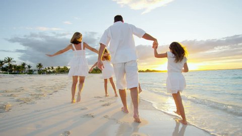 Young Caucasian parents and daughters walking on a beach at sunrise