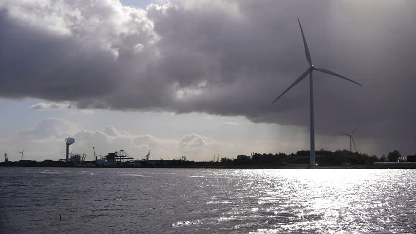Wind turbine at canal surrounded by dark clouds