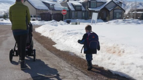 A mother walking with a stroller to pick up her boy from the bus stop and walk him back home