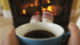 Woman drinking coffee by fireplace getting warm and cozy. Person is having refreshment during in living room. She is warming herself in front of burning stove during winter. RED EPIC SLOW MOTION.