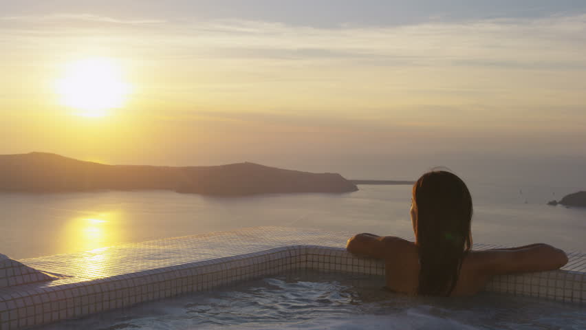 Asian woman relaxing at the edge of swimming pool at resort. Young female is watching beautiful view of sunset. She is enjoying her vacation at resort by sea. Santorini, Greece. | Shutterstock HD Video #14587372