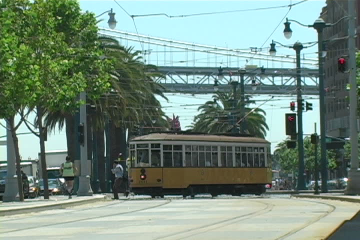 A street car passing by with the Bay Bridge in the background.