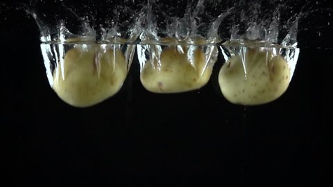 Three potatoes falling in water against black background. Super slow motion shot