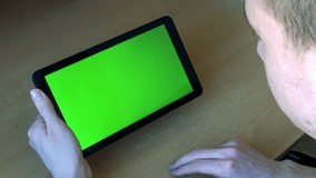 young man works on tablet in office on the table - green screen - man slides on screen 