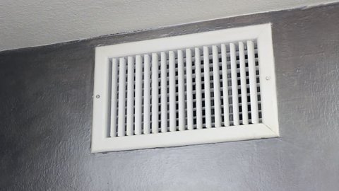 Man Examining an Air Vent. 
Mature male looking inside an upper wall white grid air duct on a gray wall near a white ceiling. A guy examining a heating and cooling air register duct for maintenance.