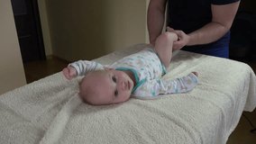 Man with infant baby doing special gymnastic exercises for body leg tonicity treatment on table. Healthy lifestyle. Closeup shot. 4K UHD video clip.