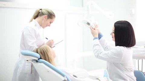 Young beautiful girl dentists examine x-ray of the patient and prepare for tooth treatment.