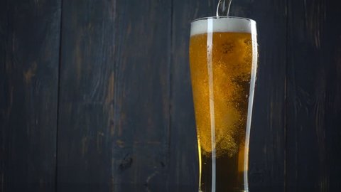 Pouring beer into glass over dark wooden background. Slow motion