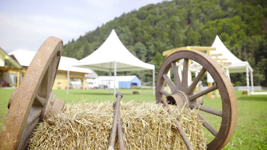Two wooden wheels lean on hay jib shot 4K. Low angle jib shot of old carriage wheels on both sides of square hay with poles in front. Countryside shot.