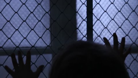 Helpless Child Shaking A Metal Fence Trying To Escape. Silhouette of children hands on the window fence. Refugees or abandoned child. Mental Institution. Family violence. Fingers on the fence