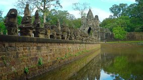 Vehicles pass along a statue lined roadway past the temple moat to an entrance of Angkor Wat in Cambodia. UHD video
