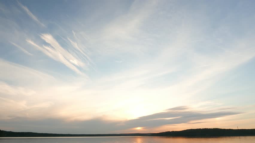 Light stretched clouds over evening sky, lake sunset skies time lapse shot. Sun disk ahead, hide behind dense stripe of clouds, move down to horizon line. Reflex on flat water Royalty-Free Stock Footage #14637331