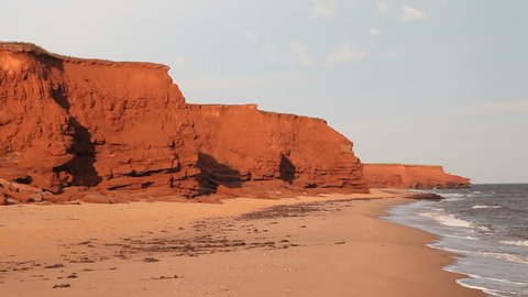 Waves rolling in on an empty beach with red sandstone cliffs on Prince Edward Island, Canada.