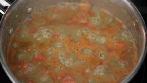 Cooking Lentil Soup with Tomatoes and Vegetables. 
Closeup of a male hand stirring lentil soup with vegetables and tomatoes cooking in a small pan, then placing a lid on it before moving his hand away