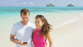 Couple on beach vacation using smart phone app. Romantic couple in love on honeymoon having fun on, Oahu, Hawaii. Couple holding smartphone. RED EPIC SLOW MOTION.