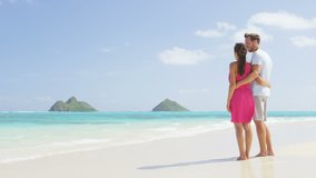Beach honeymoon couple holding hands walking on white sand beach. Newlyweds happy in love relaxing on summer holidays, Oahu, Hawaii, USA with Mokulua Islands. Travel vacation concept.