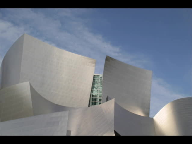 A shiny contemporary building reflects fast moving clouds in a blue sky.