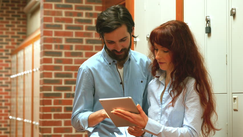 Two happy students using a tablet in a hallway