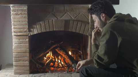 sad and mounrful guy sat in front of a fireplace