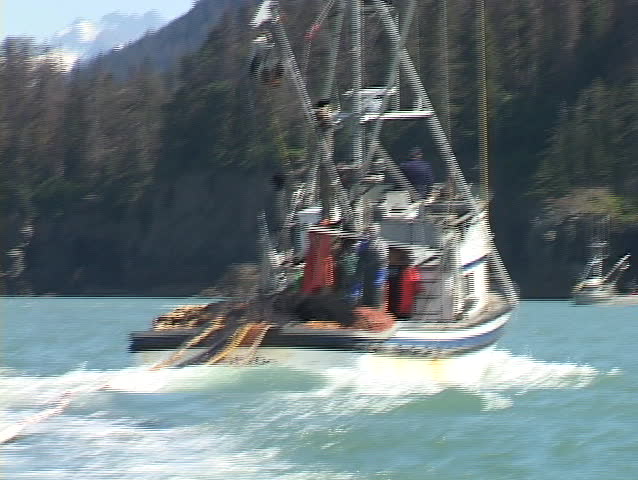 A fisherman watches as a large net is cast into the ocean from the back of his boat.