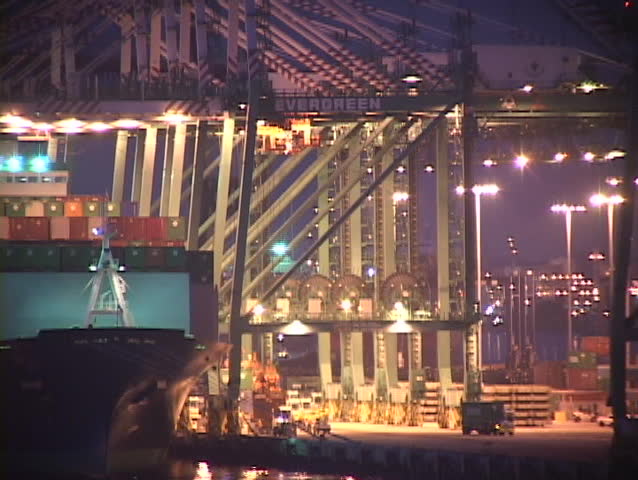 Medium shot of giant cargo container ship entering a port at night.