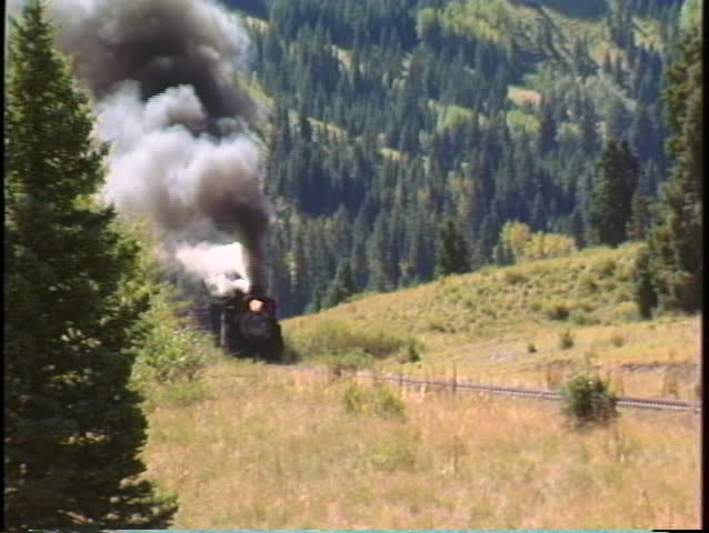 Pan-right shot of a steam freight train chug through the Colorado mountains.