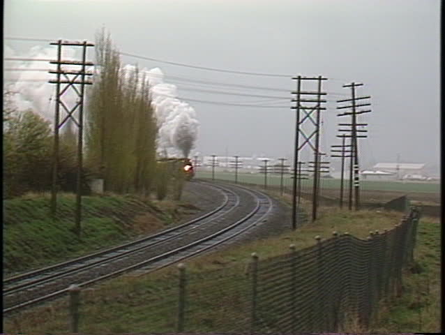 Following shot of a steam passenger train rounding a bend.