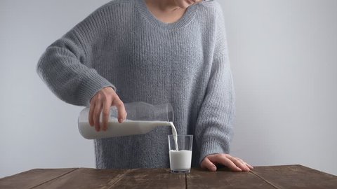 Cinemagraph loop Unrecognizable woman in cozy warm sweater pours milk from vintage bottle to glass on old wooden table for breakfast Isolated on white Adlı Stok Video