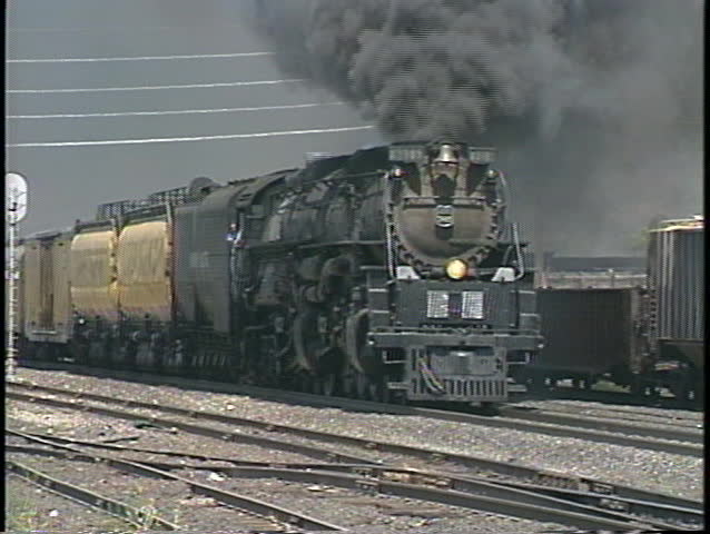 Tracking shot of a steam train passing through a freight yard.