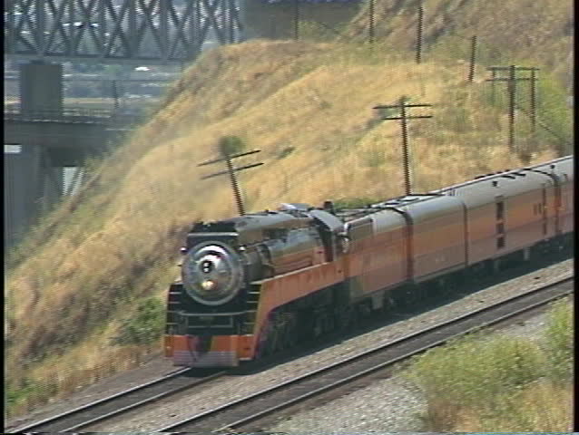 Zoom-out of a Southern Pacific train passing by a large highway bridge.