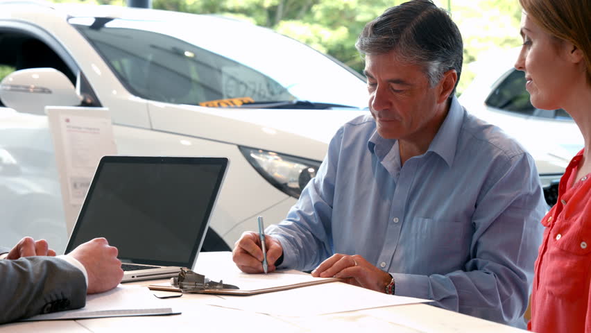 Businessman siging some documents at the car showroom