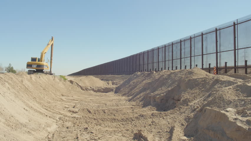 Wide of a trench near the border fence with heavy equipment in frame.