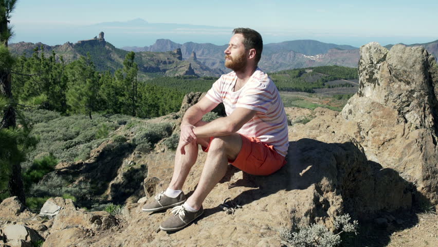 Man sitting on the rock in mountains and relaxing on the sun
