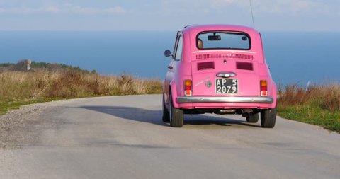 ALTIDONA, ITALY - FEBRUARY 20, 2016: Old pink Fiat Nuova 500 city car running in the street with cloudy blue sky. Produced by the Italian manufacturer Fiat between 1957 and 1975.