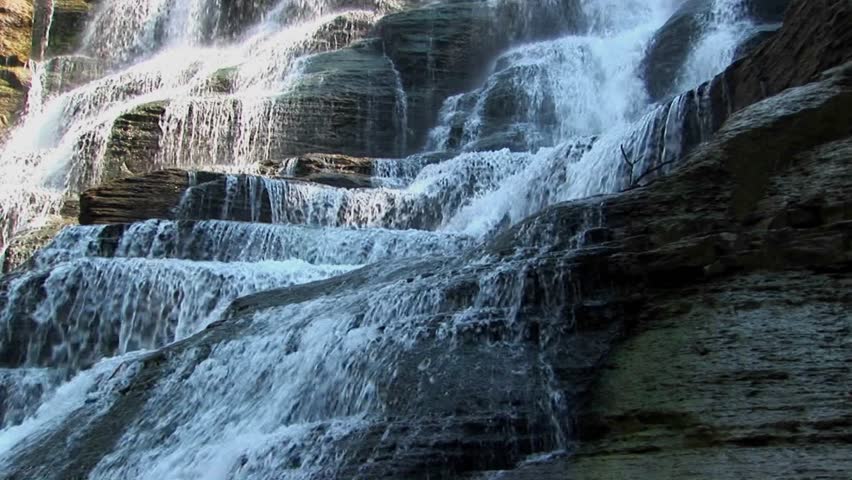 A wide waterfall flows over rock ledges in Ithaca Falls, New York.