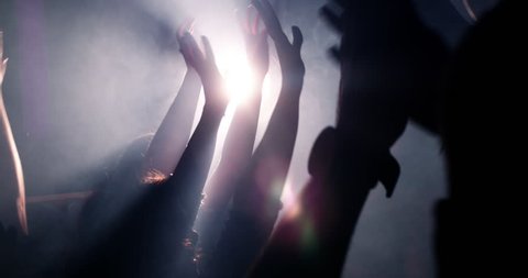 Slow mortion shot of young festive people with their hands raised and in the air at concert or party. Smoke is lingering in the nightclub and silhouettes of teenagers dancing.