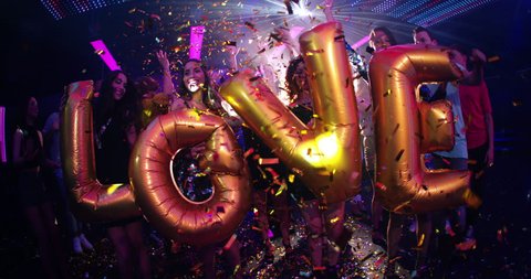 Happy dancing cheerful people holding balloons saying love in the modern hip nightclub while streamers are flying aound and everyone is having a good time