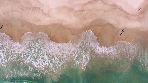 Top down aerial view of ocean waves breaking on the beach with people walking by in Rio de Janeiro, Brazil.