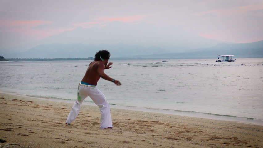 Brazilian capoeira dancer training on the beach at sunrise.