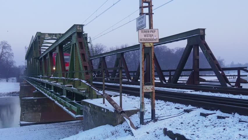 Fraight Train, Modern Red Locomotive, Tanks are Moving by Old Railroad Bridge through a River, Bridge with Metal Constructions, Panorama, Wintery Landscape, snow is on a ground, bare branches trees,