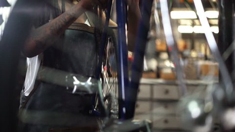 Afro-american woman with dreads and tattoos fixing a bicycle wheel in her repair workshop where she works as a skilled bike mechanic