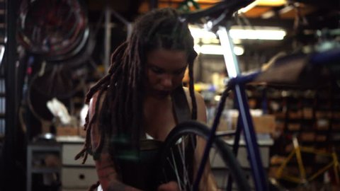 Hipster female bicycle mechanic with dreadlocks and tattoos working on a bicycle in her repair workshop