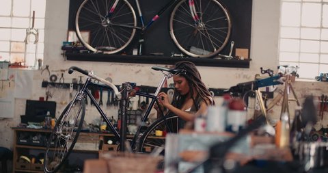 Afro-american craftswoman repairing a bicycle in her bike repair workshop with tools and spares around her