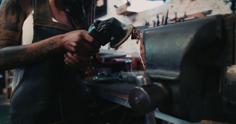 Cropped closeup of a woman mechanic in a workshop grinding a piece of metal with sparks flying