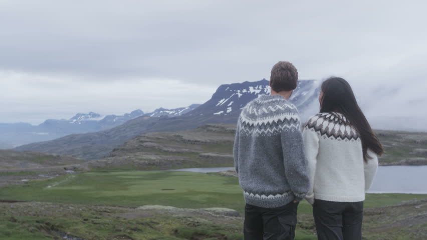 People looking at view of mountains on Iceland wearing Icelandic sweaters in amazing landscape. Woman and man model enjoying healthy outdoors lifestyle. RED EPIC 96 FPS.